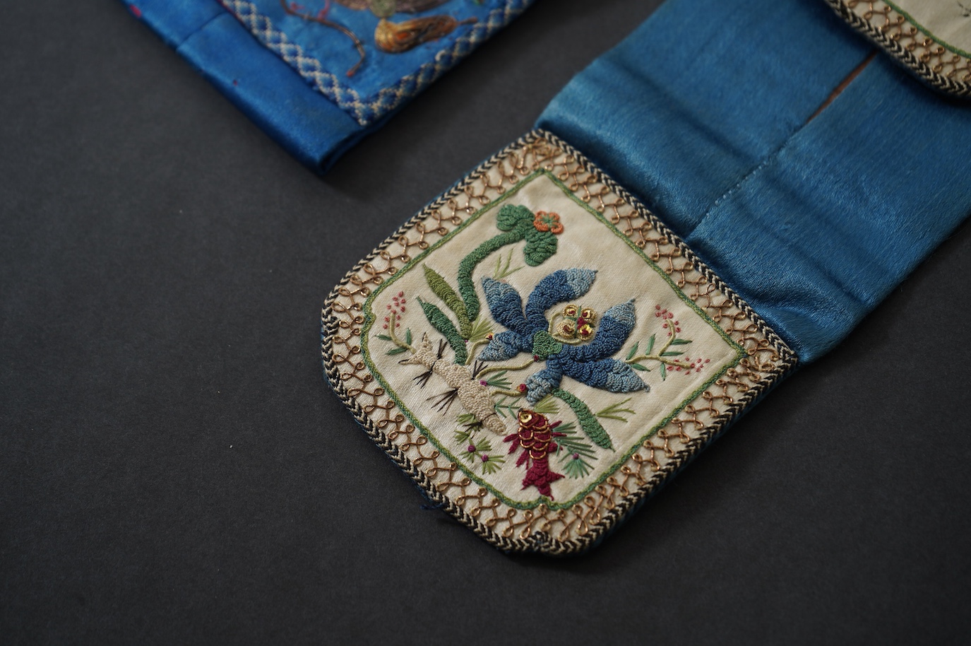 Two Chinese late Qing Dynesty coloured silk and gold thread embroidered belt purses, or ‘hebao’, for carrying coins, seals and fragrant herbs etc. One - 19cm long,in cream silk, with the embroidered words: “It’s music is